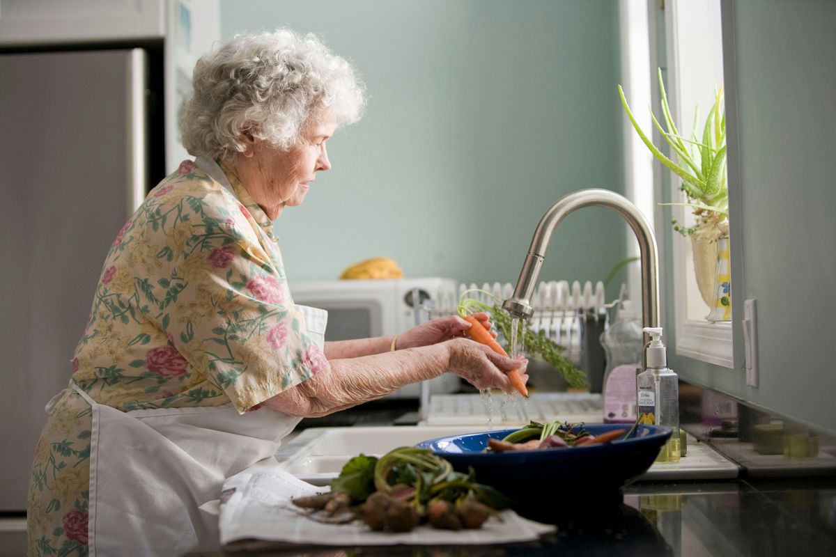Elderly woman washing vegetables alone